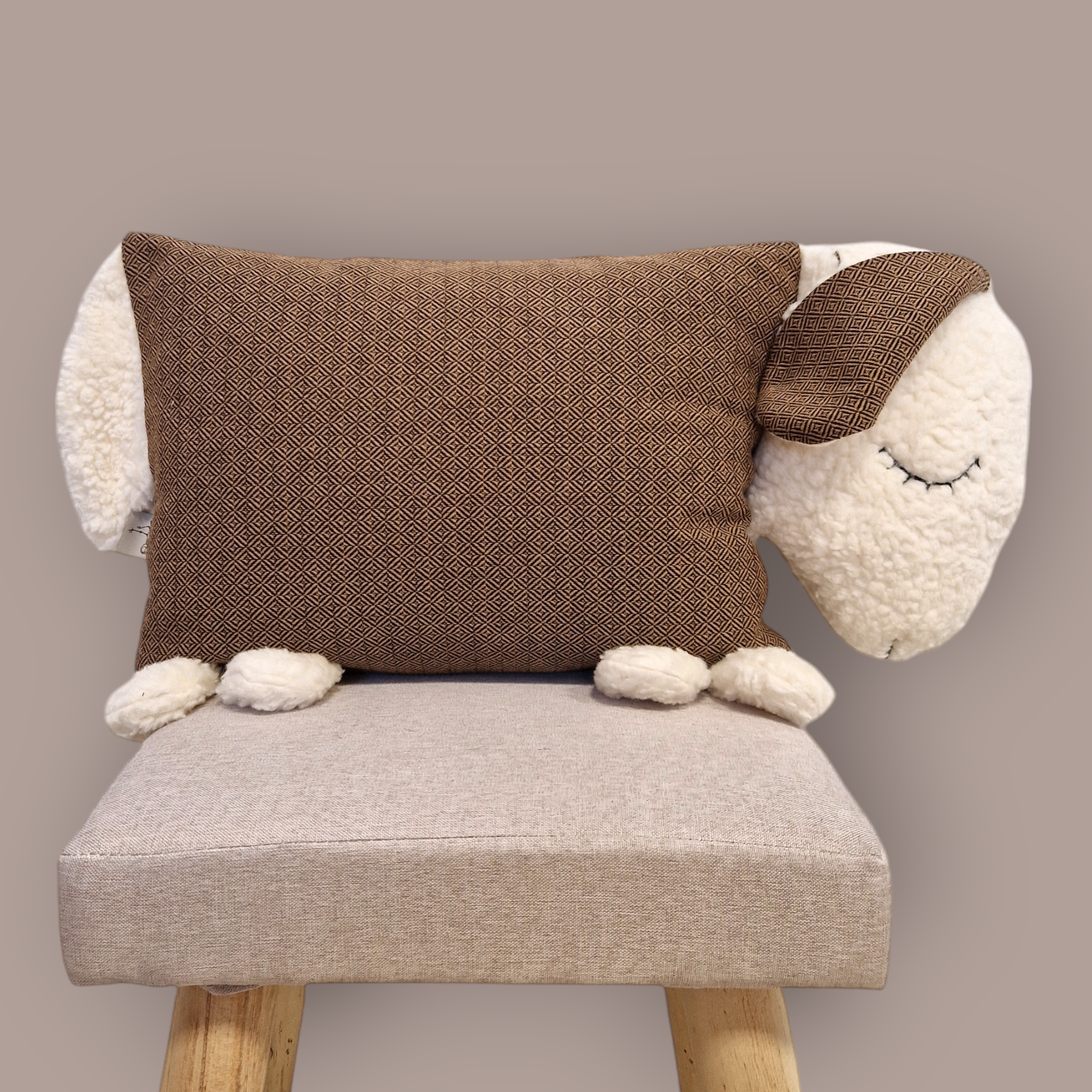 Kuschelschaf Leo Cafe plush toy on a beige chair with woven fabric and cotton fleece elements.