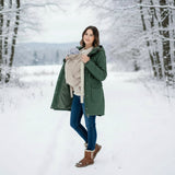 Frau trägt Baby mit beige Storchenwiege Tragecover im winterlichen Schneelandschaft