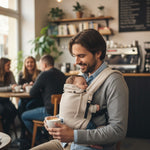 Vater trägt Baby in Valeno Mondstein Babytrage gemütlich im Café.