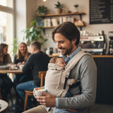 Vater trägt Baby in Valeno Mondstein Babytrage gemütlich im Café.