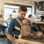 Vater trägt Baby in Valeno Sand Babytrage mit gepolsterten Trägern und Dreipunkt-Sicherheitsschnalle in Café-Umgebung